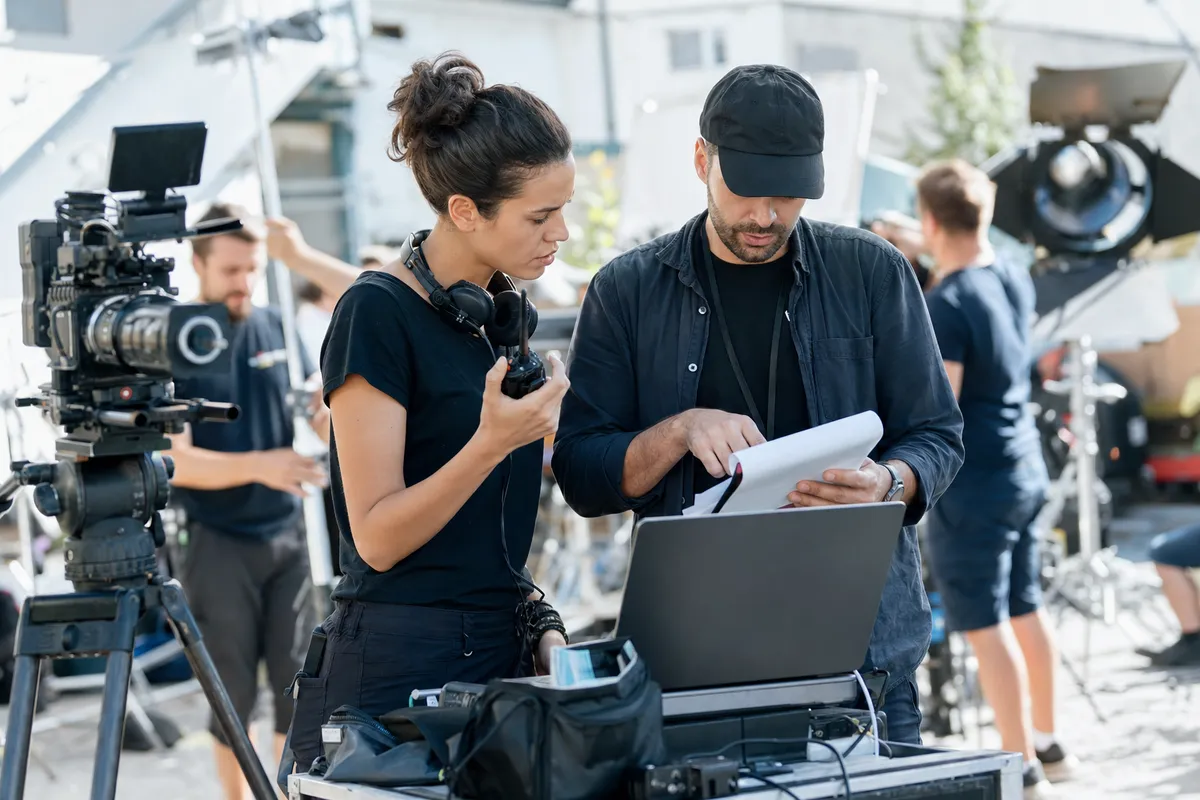 Assistant director and production coordinator reviewing a call sheet approval checklist on set before sending it to crew