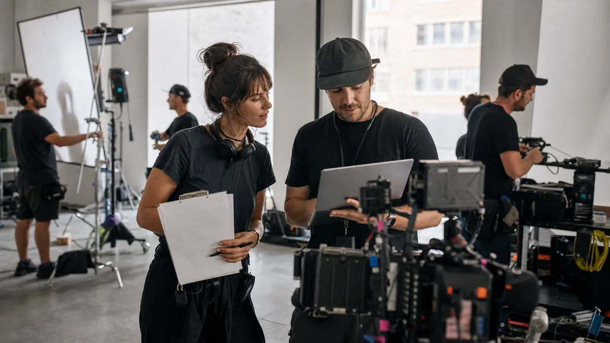 Assistant director and production coordinator coordinating a small crew with a laptop, clipboard, radios, and camera gear before call time