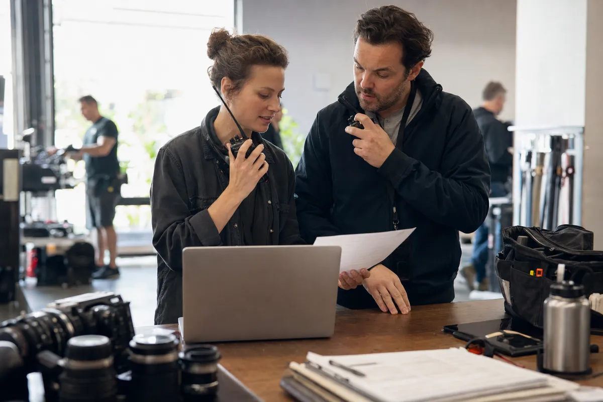 Production coordinator and assistant director coordinating crew call sheet details before a commercial shoot