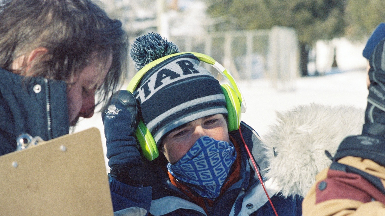 An assistant director holding a walkie-talkie and tablet coordinating crew during an afternoon split call transition on a film set.
